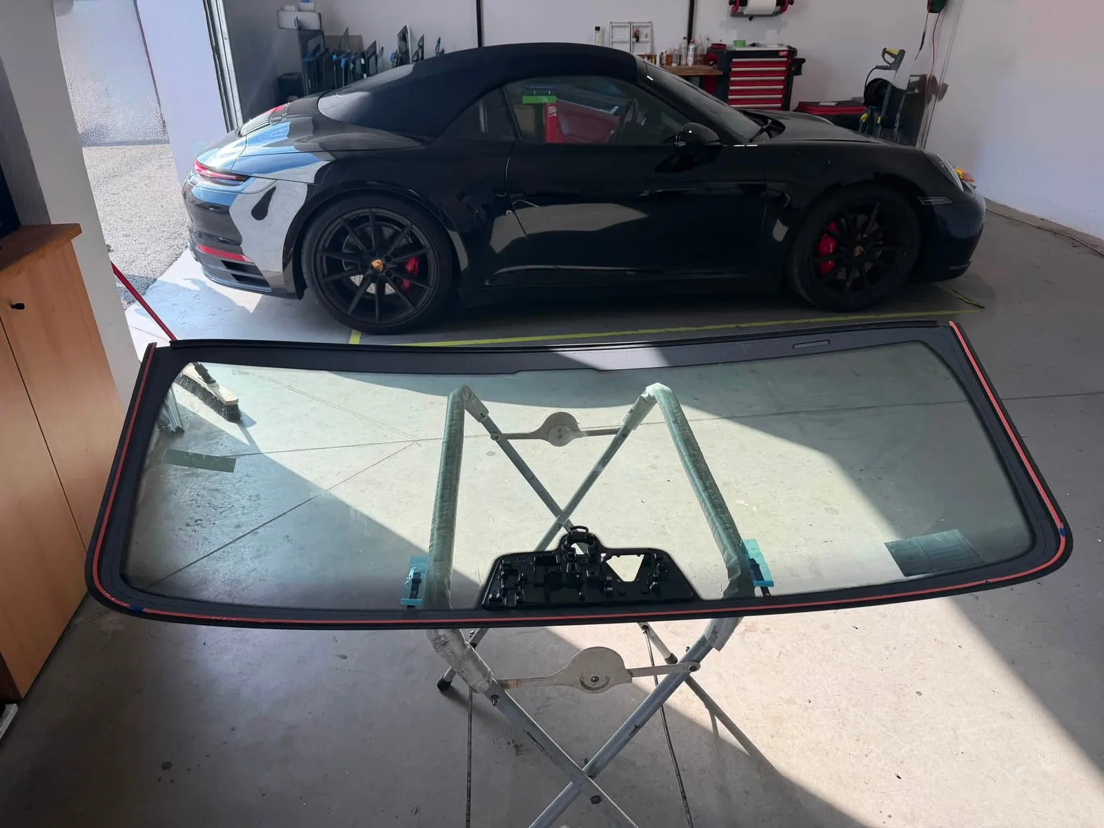 Porsche 911 Cabriolet — Parbrizul nou, pe stand, gata de montaj. Mașina așteaptă în spate.